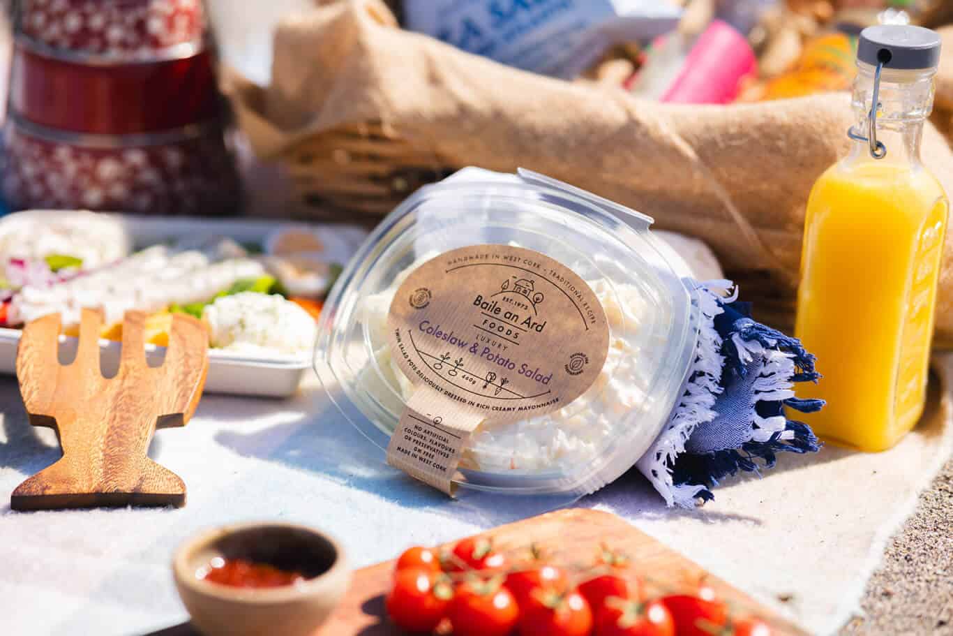 Coleslaw and potato salad, orange juice, tomatoes on picnic blanket.